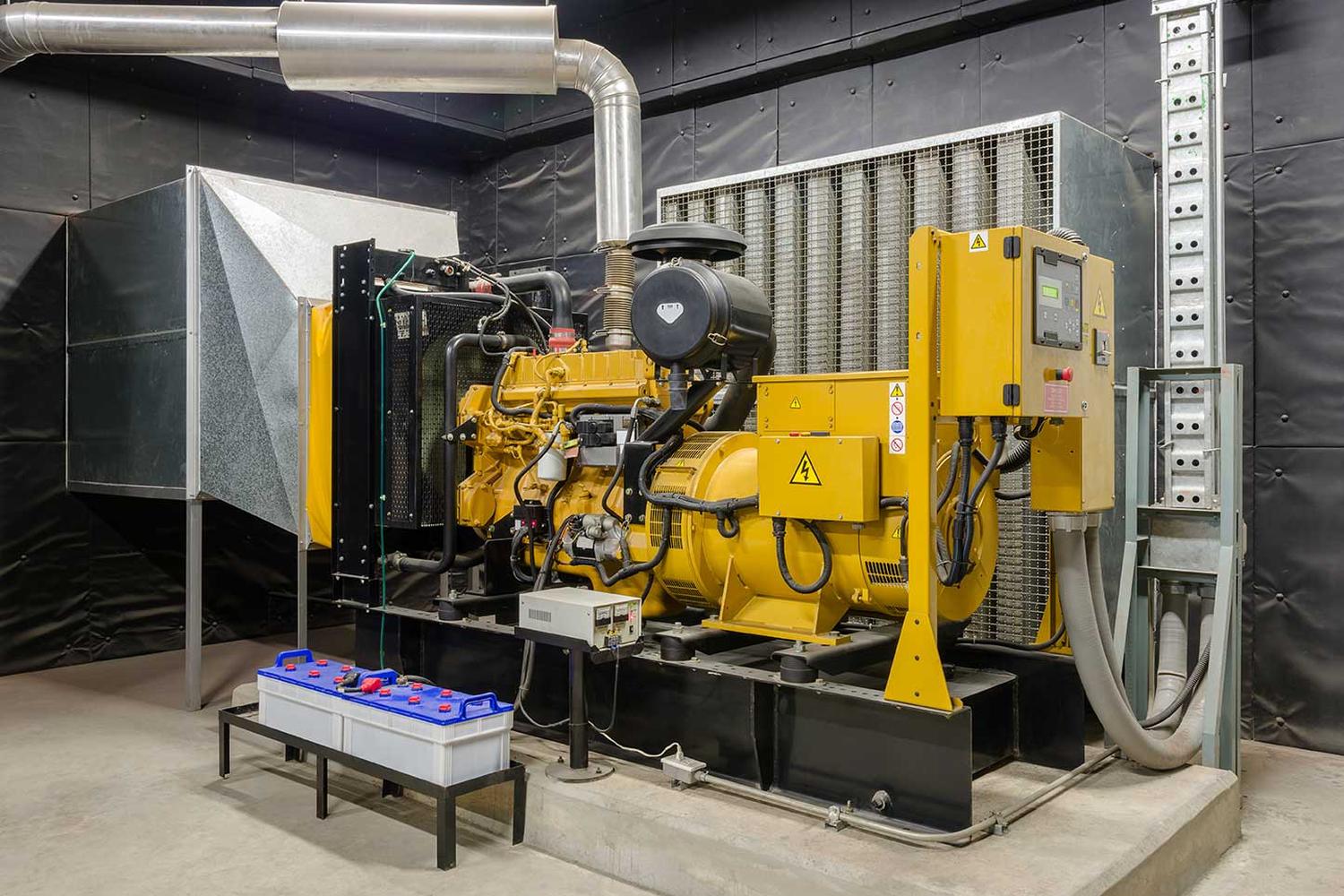 A standby diesel generating set in a plant room, showing the engine, alternator, control cubicle, exhaust and battery bank